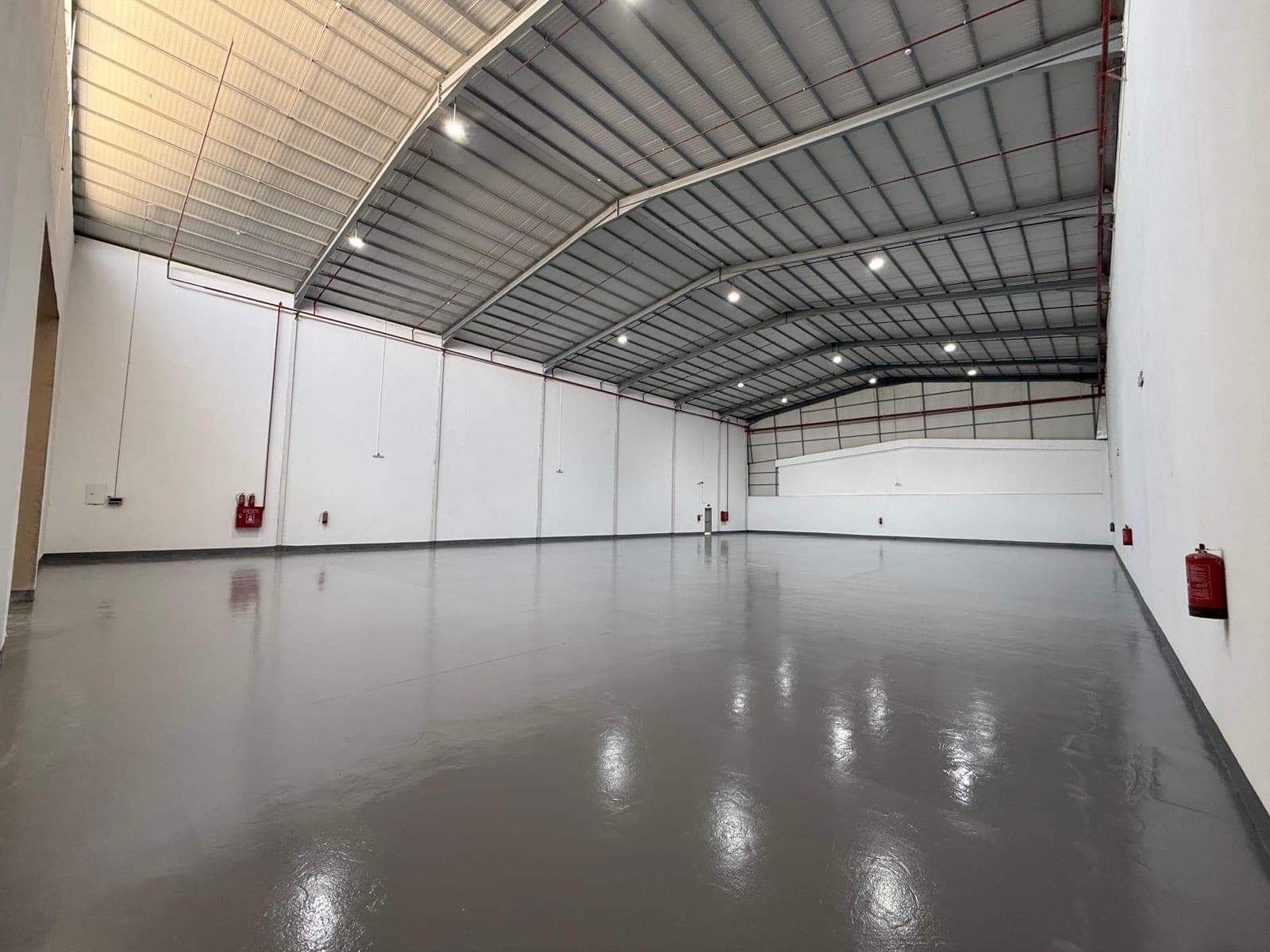 Empty warehouse with a glossy epoxy floor, arched steel roof and LED lighting